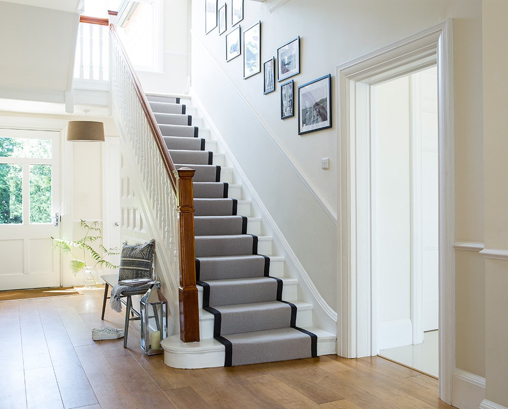 An image of a staircase - a white wooden staircase is topped with a contemporary black-edged carpet runner in grey.